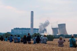 一个事业d of people watch from a distance as the iconic cooling towers of Didcot A coal power station are demolished