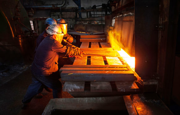 A hot steel billet is removed from furnace as a cold billet waits in foreground