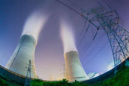 Upward view of the cooling towers and high voltage power transmission tower at night.