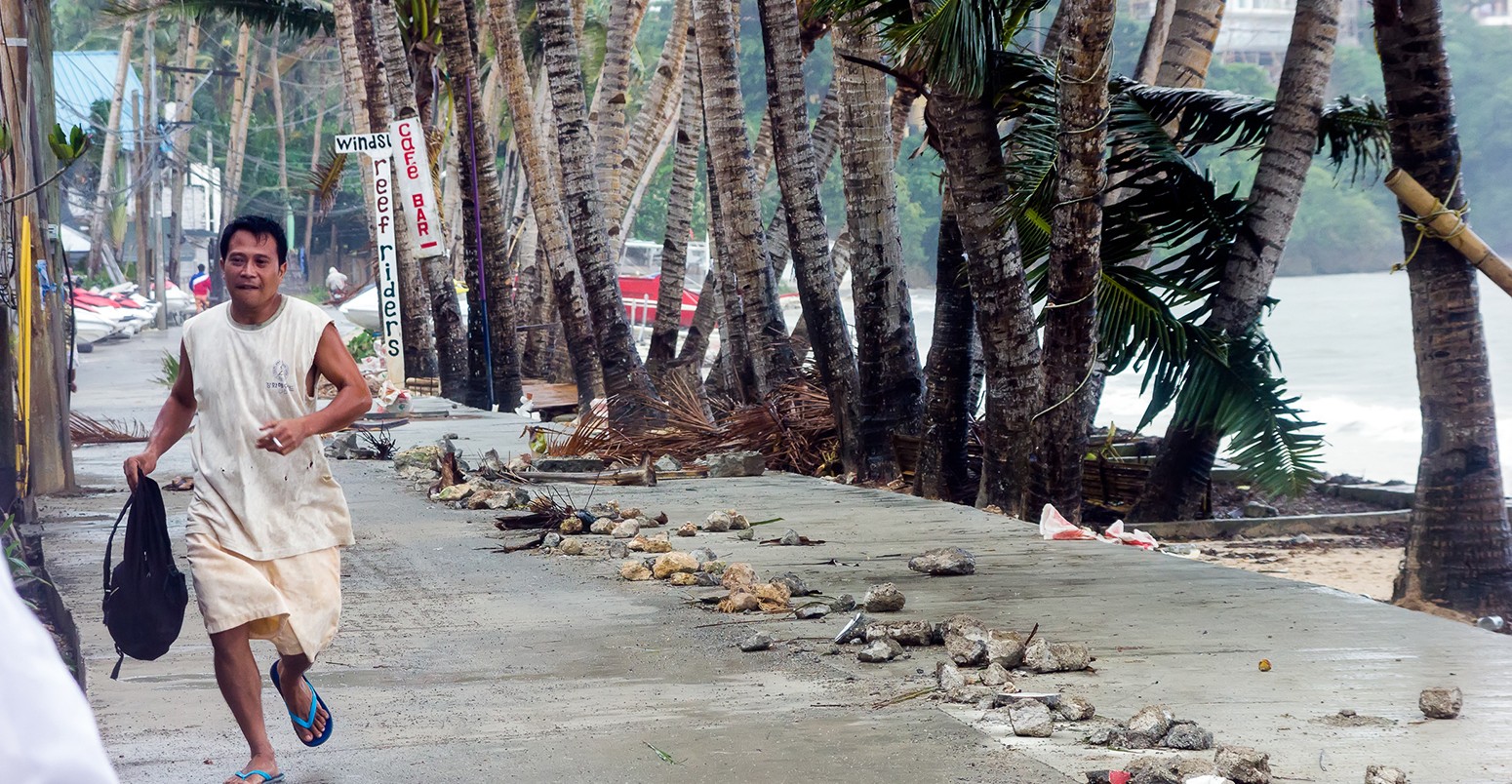 A man runs from the seafront as Super Typhoon Haiyan / Yolanda slams into the east coast sending palm trees, metal and rocks through the air