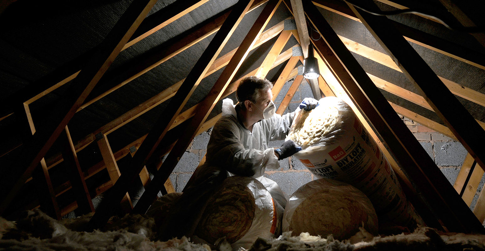 BCMCX8 MAN INSULATING A DOMESTIC HOUSEHOLD LOFT WITH ROLLS OF LOFT INSULATION UK