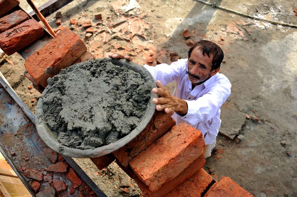 CR57BE Man lifting pan with cement onto a scaffold, construction of brick houses for families whose houses were destroyed during the during the flood catastrophe of 2010