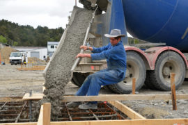 EFA7E6 builder directs wet concrete from a cement truck into the foundations of a large building.