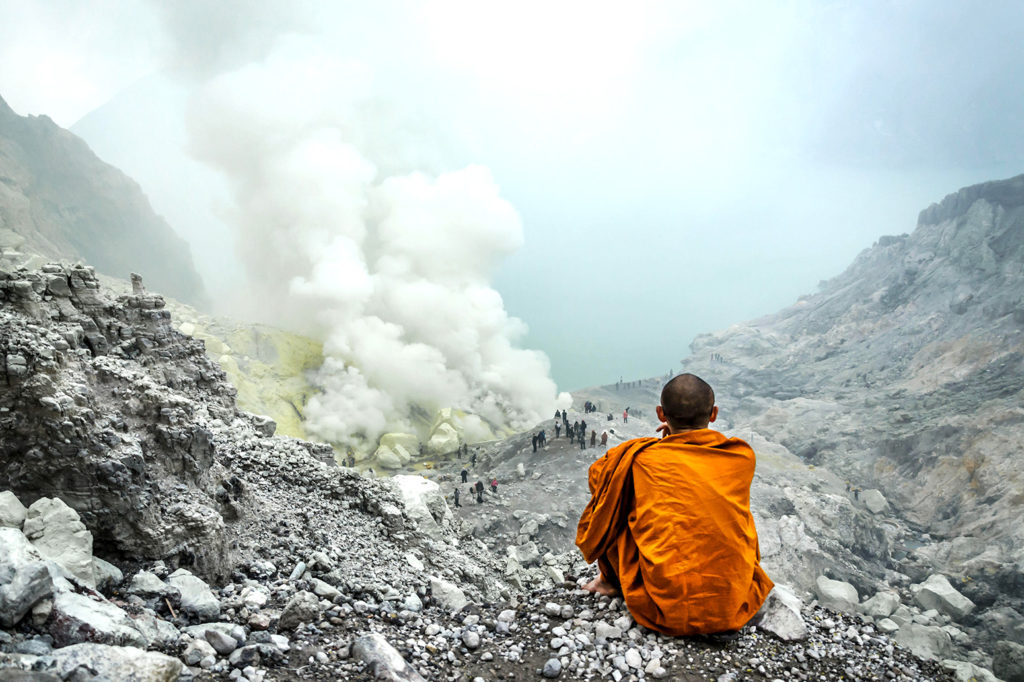 A Buddhist monk sits in front of the Kawah Ijen volcanic crater as sulphur gases are released, east Java, Indonesia. Credit: Malgorzata Drewniak / Alamy Stock Photo. PWKK7E