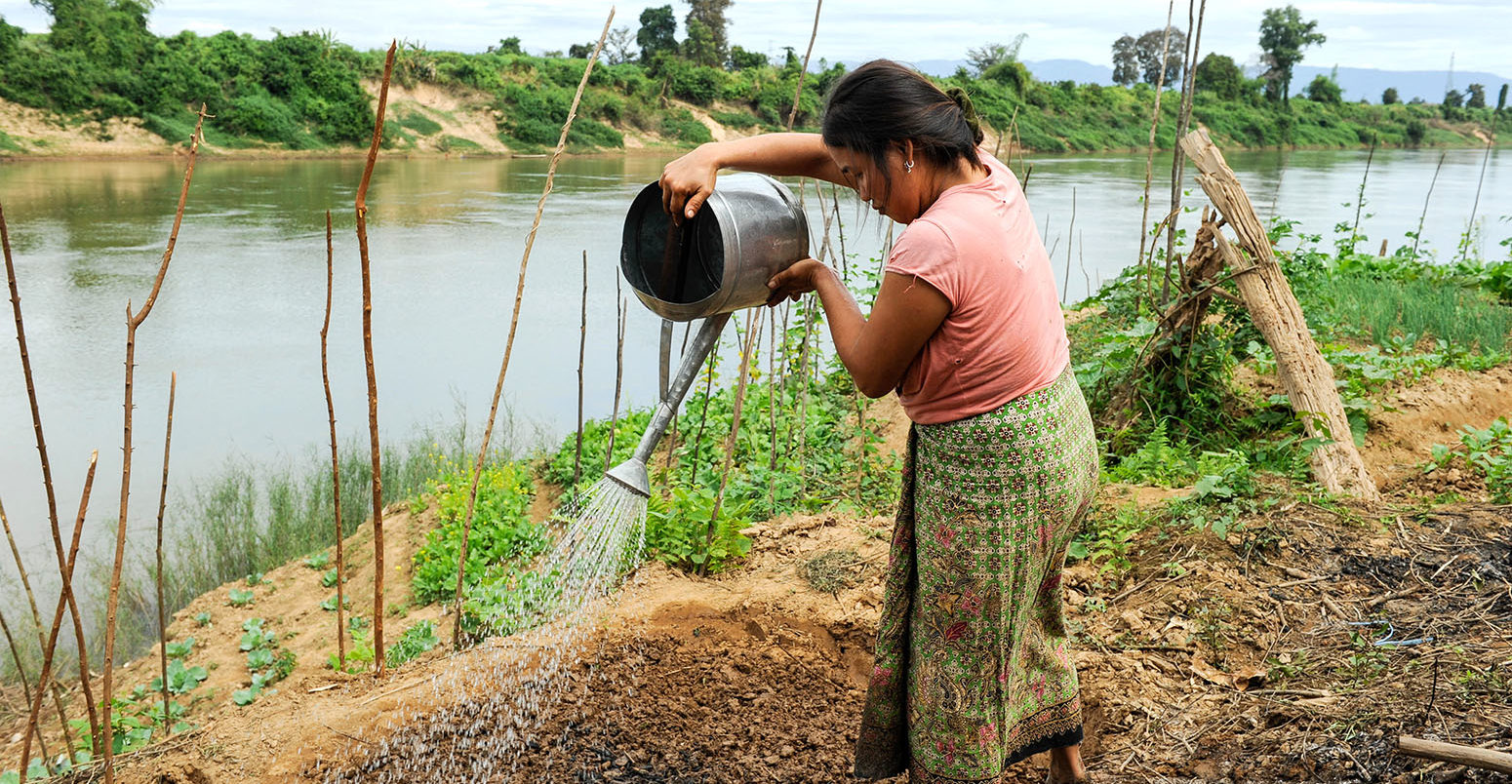 A woman waters her crops near a river in Vientiane, Laos. Credit: Joerg Boethling / Alamy Stock Photo. W18X5B