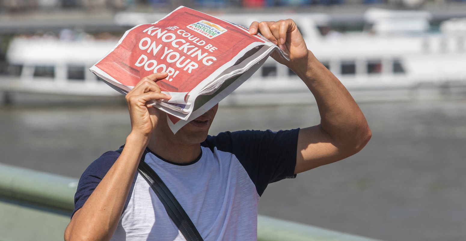 A pedestrian on Waterloo Bridge shelters with a newspaper from the sun. 25 July 2019, London.