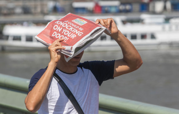 在waterloo桥梁庇护所的步行者与从太阳的一份报纸。2019年7月25日，伦敦。