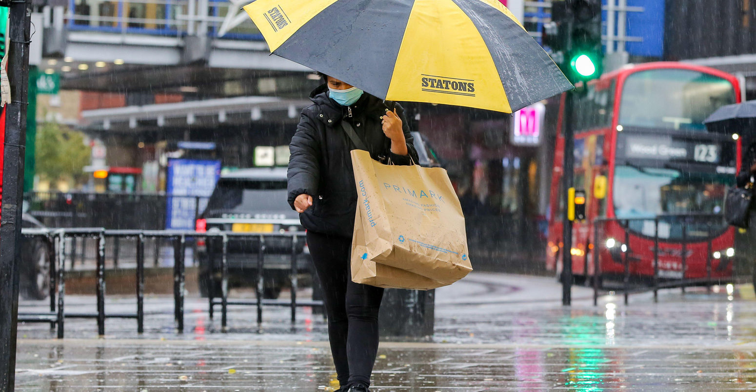 A-shopper-wearing-a-face-mask-shelters-from-the-rain-underneath-an-umbrella-on-a-wet-and-windy-day-caused-by-Storm-Alex