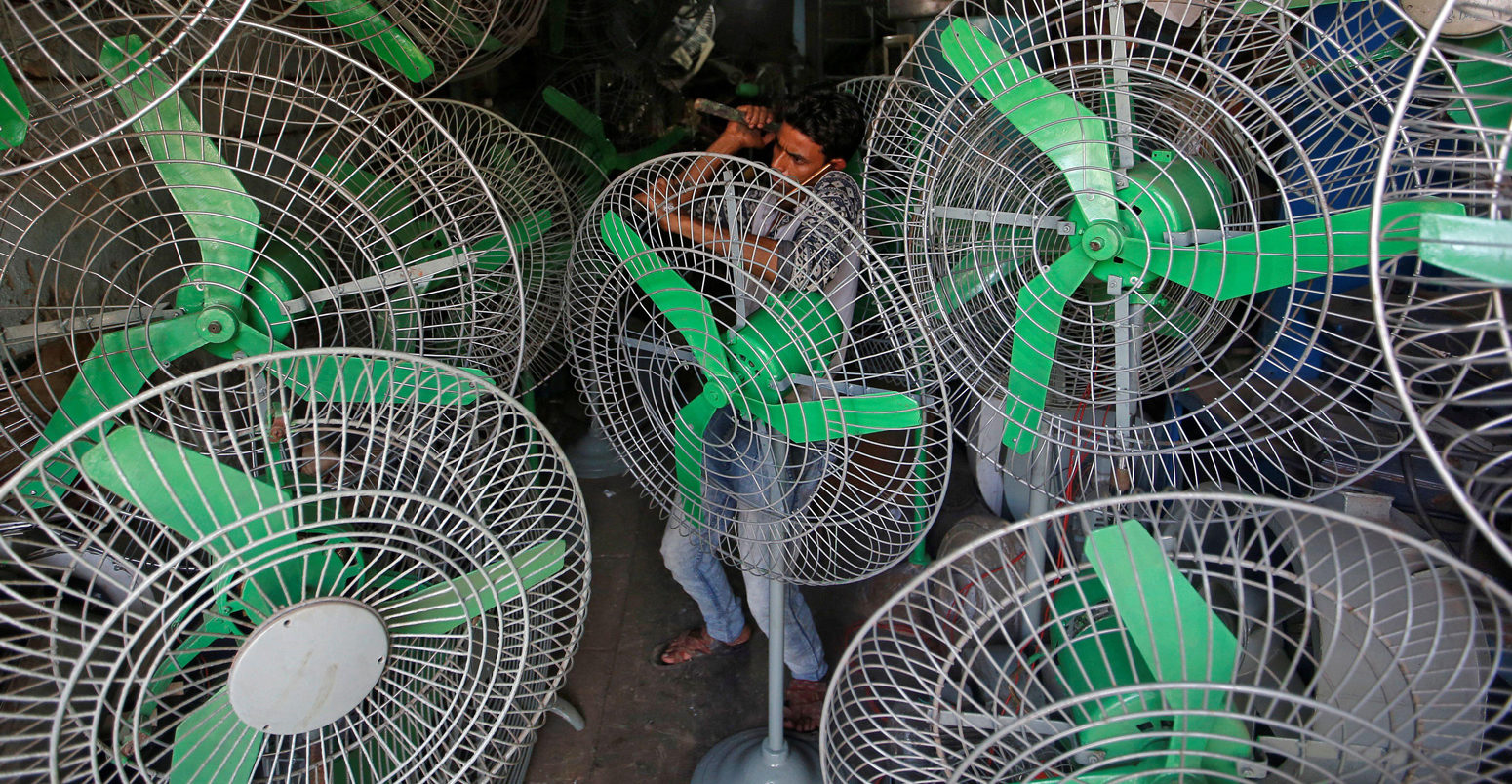 A mechanic uses a hammer to fix steel guard of an electric fan inside a shop in Mumbai