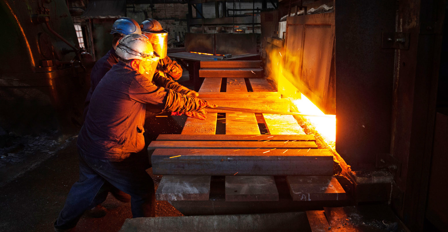 A hot steel billet is removed from furnace as a cold billet waits in foreground