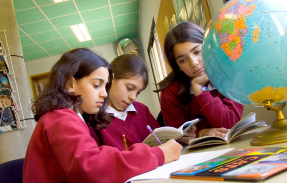 三名初中女生在学校图书馆学习地理研究全球地图集