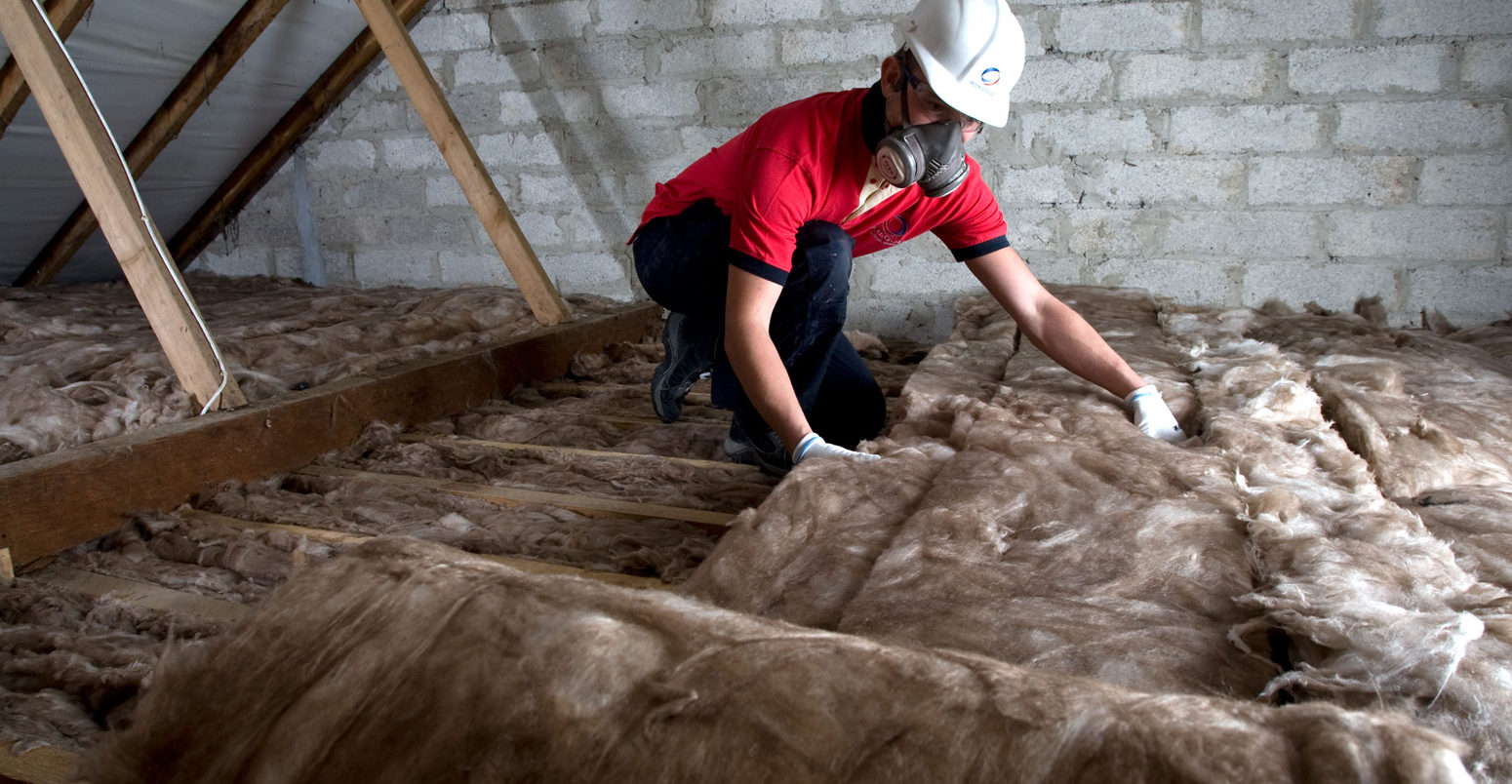 A worker lays loft insulation in the attic of a residential property in Cornwall, UK