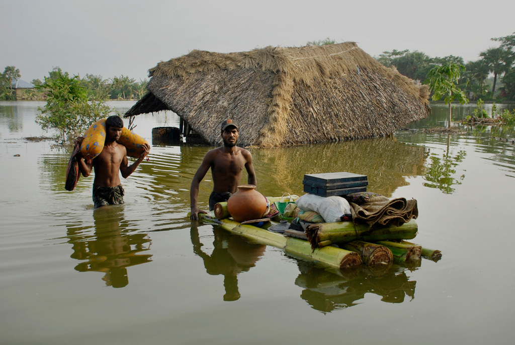 Men with their belongings leave their flooded hut after cyclone Aila hit Bangladesh