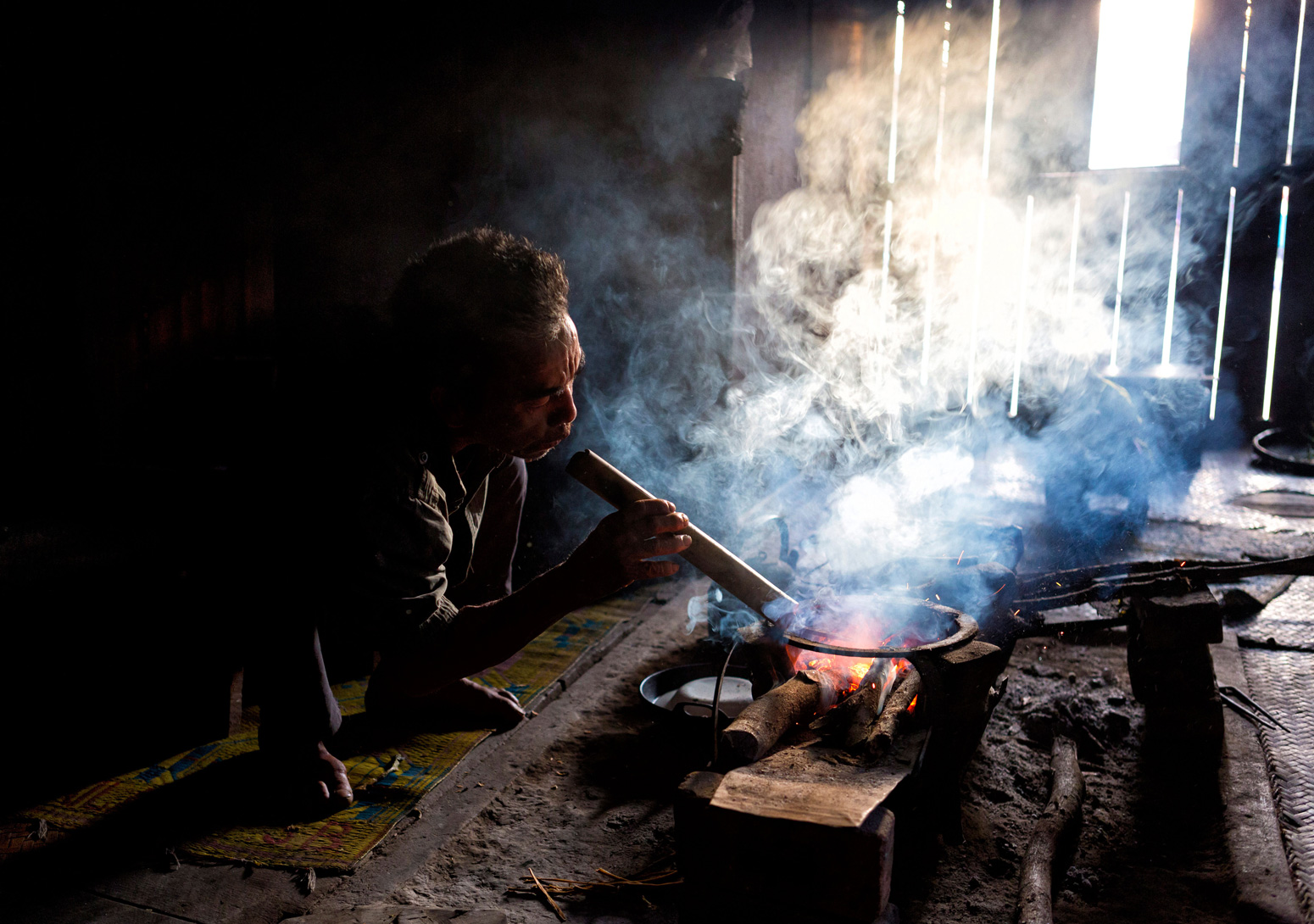 Man from the Palaung tribe cooking on open fire in a village near Kengtung, Burma
