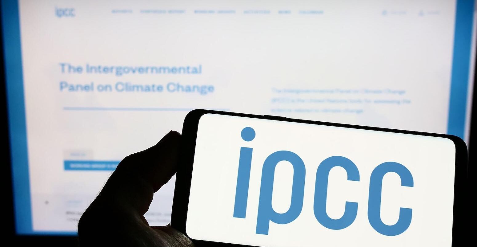 Person holding smartphone with logo of Intergovernmental Panel on Climate Change (IPCC) on screen in front of website. Focus on phone display.