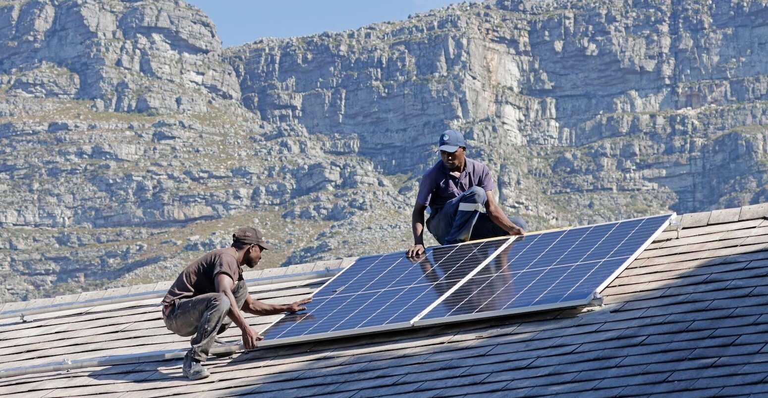 Two men install a solar panel on a roof in South Africa.