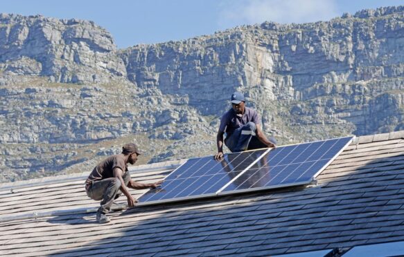 Two men install a solar panel on a roof in South Africa.