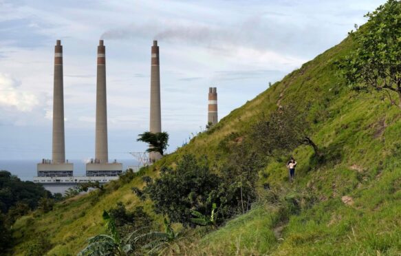 A couple walk on a hill as the chimneys of Suralaya coal power plant in Indonesia loom in the background.