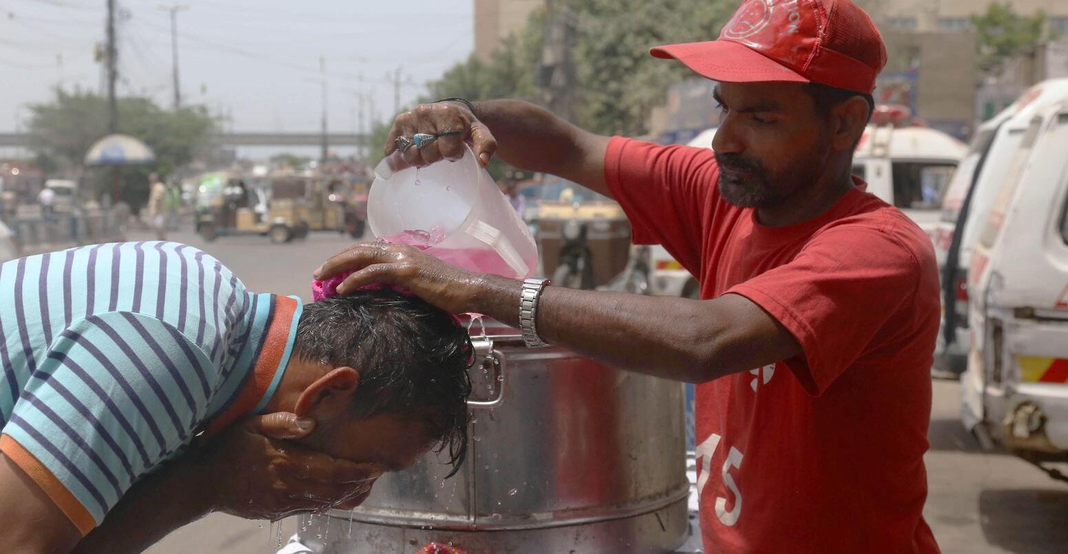A volunteer pours water on a pedestrian during a heatwave in Karachi, Pakistan, 2022. Image ID: 2J8JH4E.