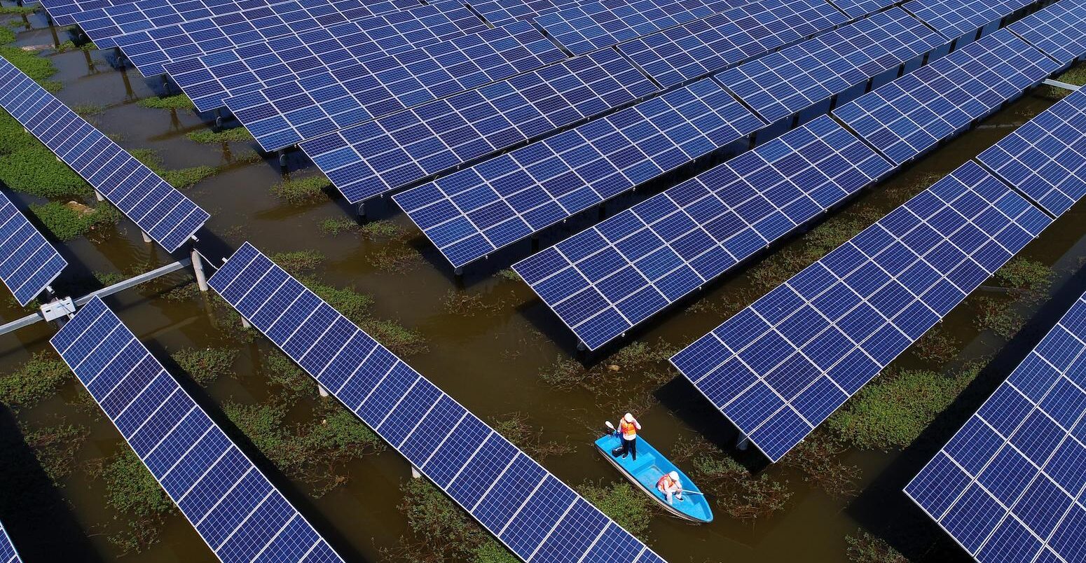 Workers boat past solar panels in a floating solar energy farm in Jingzhou, China. Image ID: W791EX.
